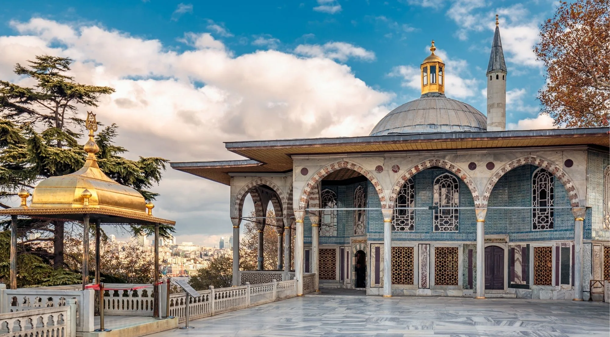 The Baghdad Kiosk and the gilded Iftariye canopy on the marble terrace at Topkapi Palace at golden hour, with Istanbul behind