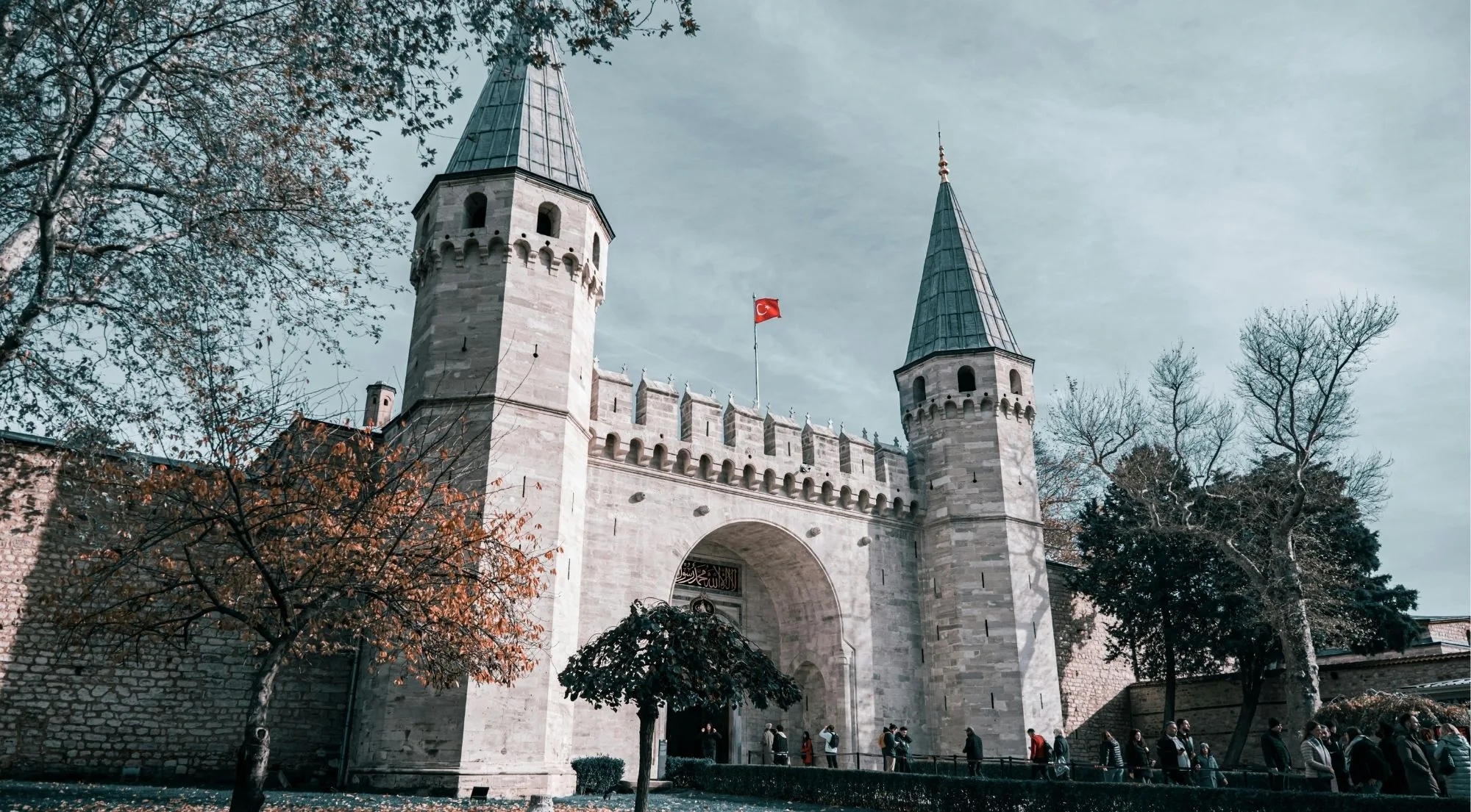 Visitors queuing at the Gate of Salutation at Topkapi Palace under a grey autumn sky with bare trees