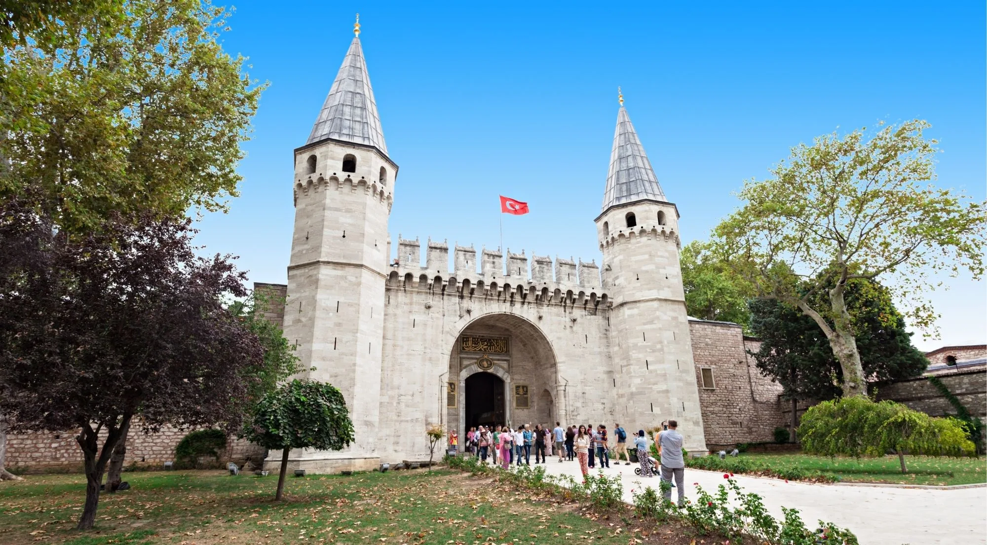 The twin conical towers of the Gate of Salutation at Topkapi Palace, with a Turkish flag flying above the crenellated wall
