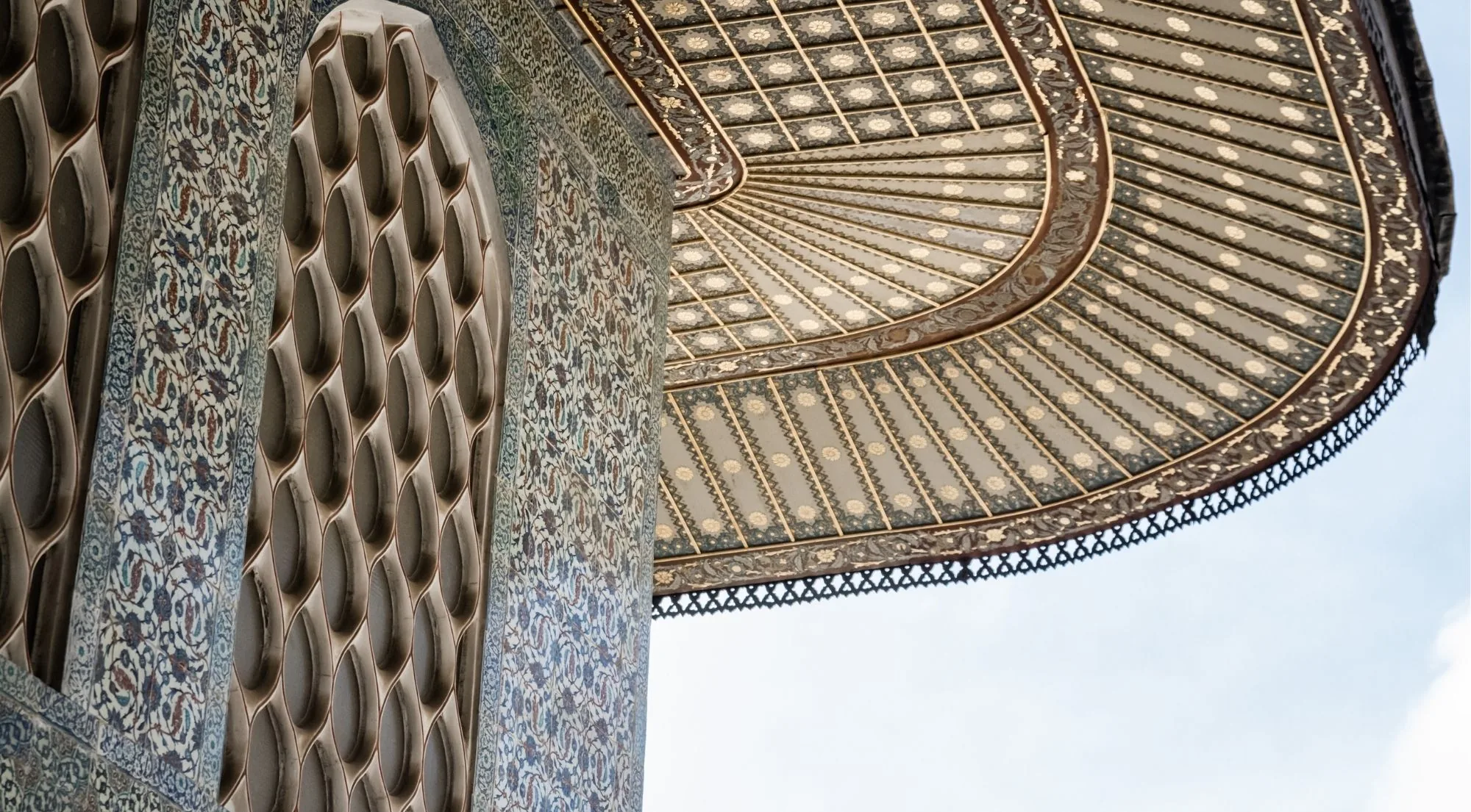Looking up at the gilded underside of the Iftariye canopy at Topkapi Palace beside a tiled muqarnas arch