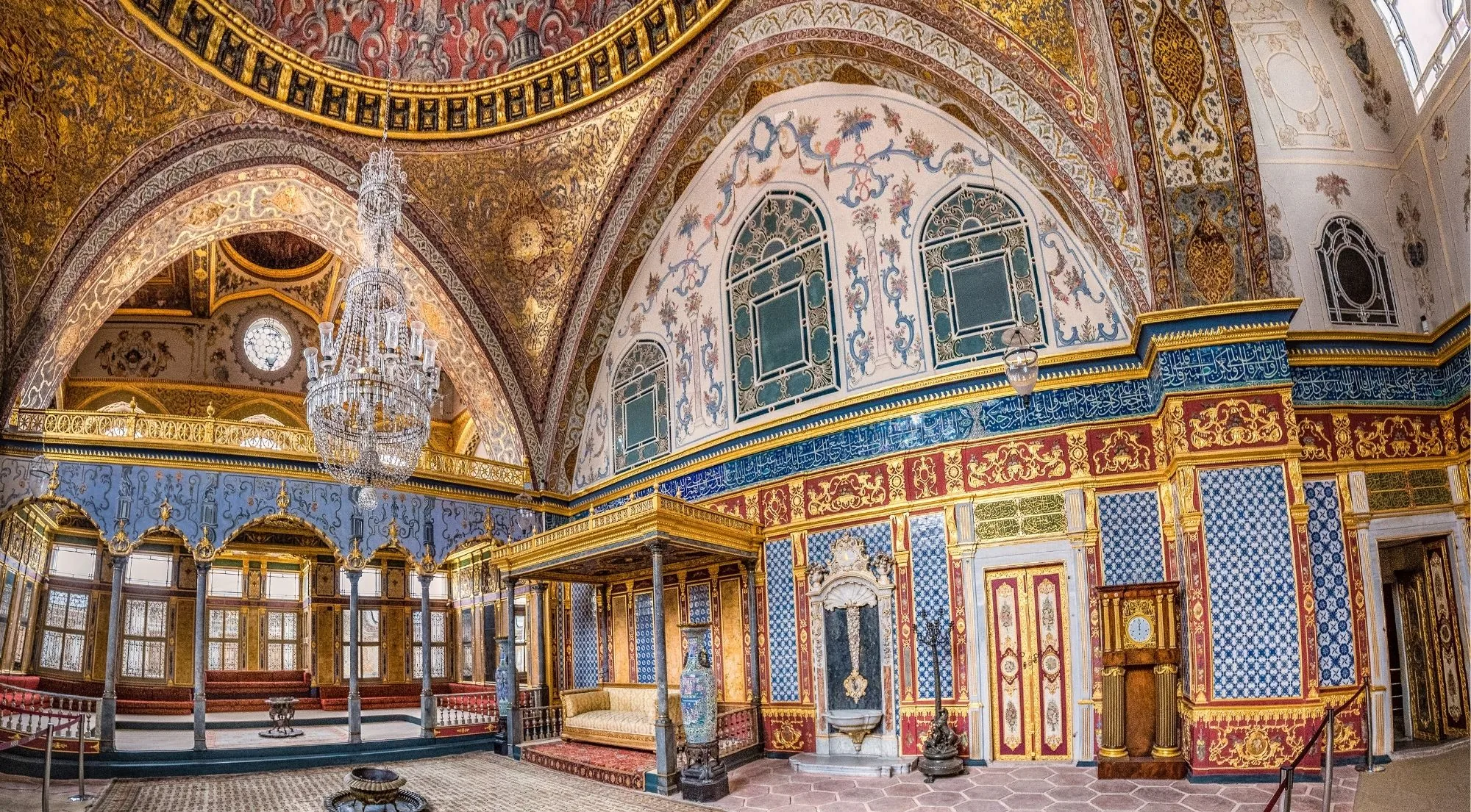 The domed Imperial Hall inside the Topkapi Harem, painted in gold, blue and red with a crystal chandelier above a tiled floor