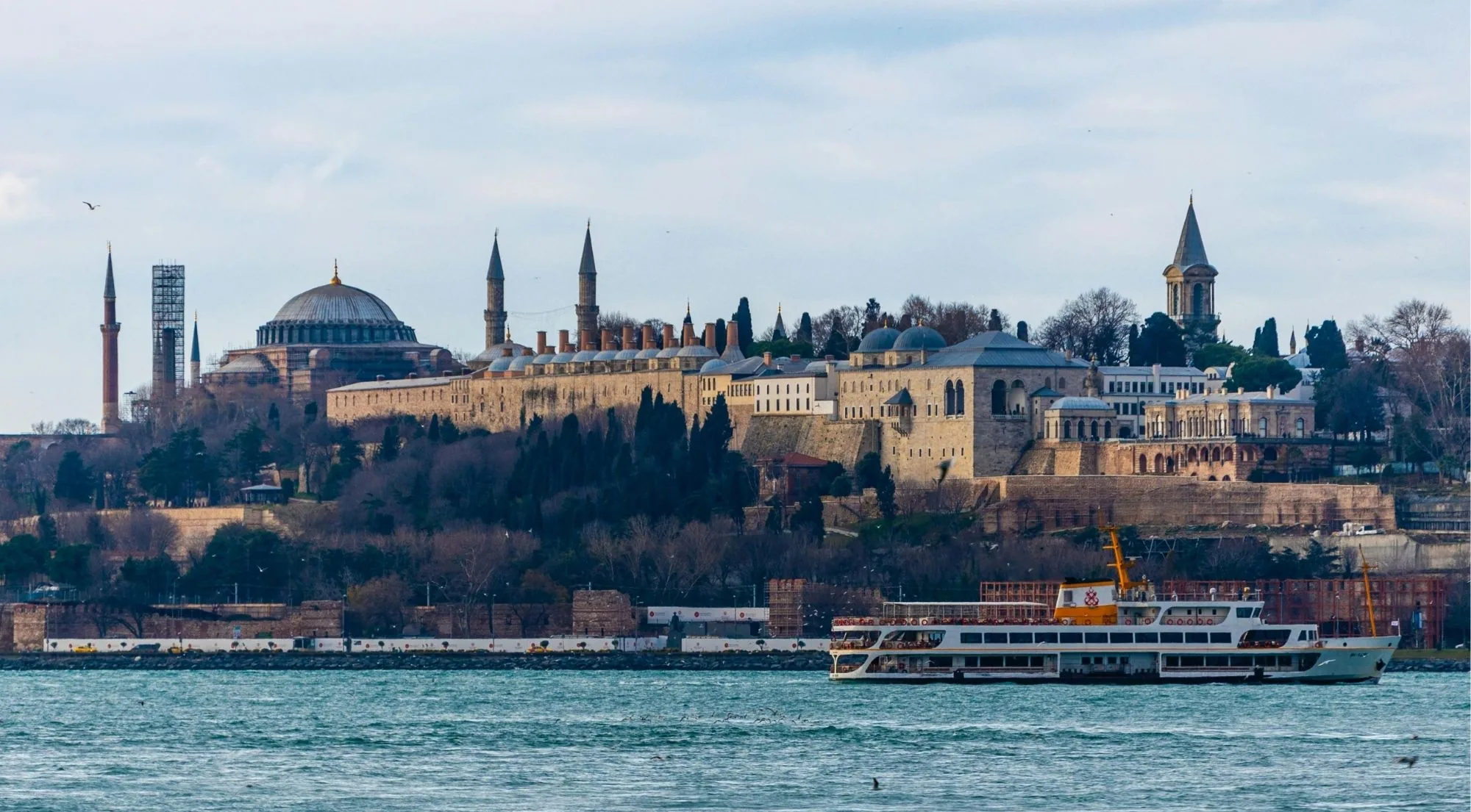 Topkapi Palace seen from the water, its domes and the Tower of Justice rising above the sea walls as a passenger ferry passes