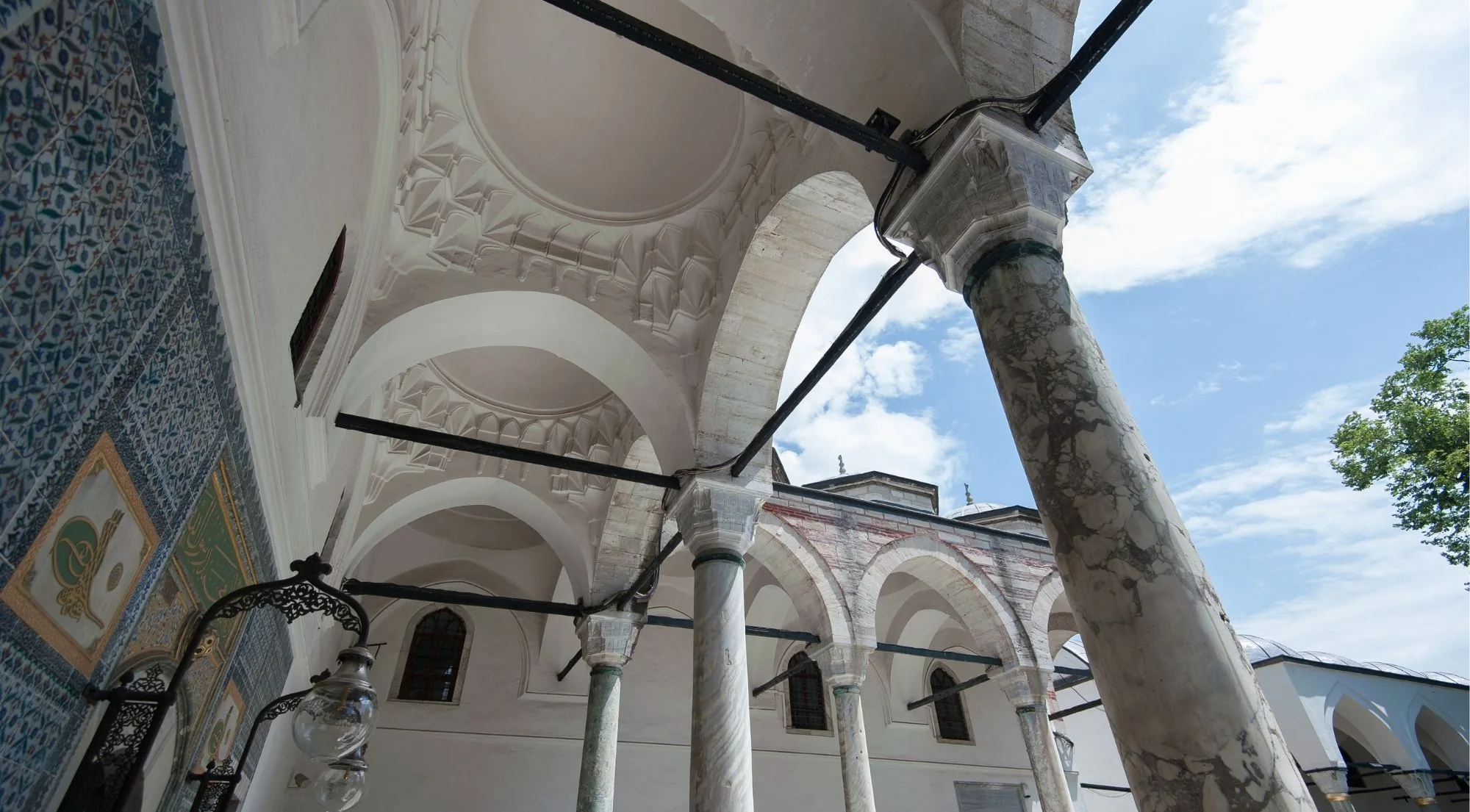Marble columns and a vaulted white portico beside a tiled wall in the courtyards of Topkapi Palace, seen from below