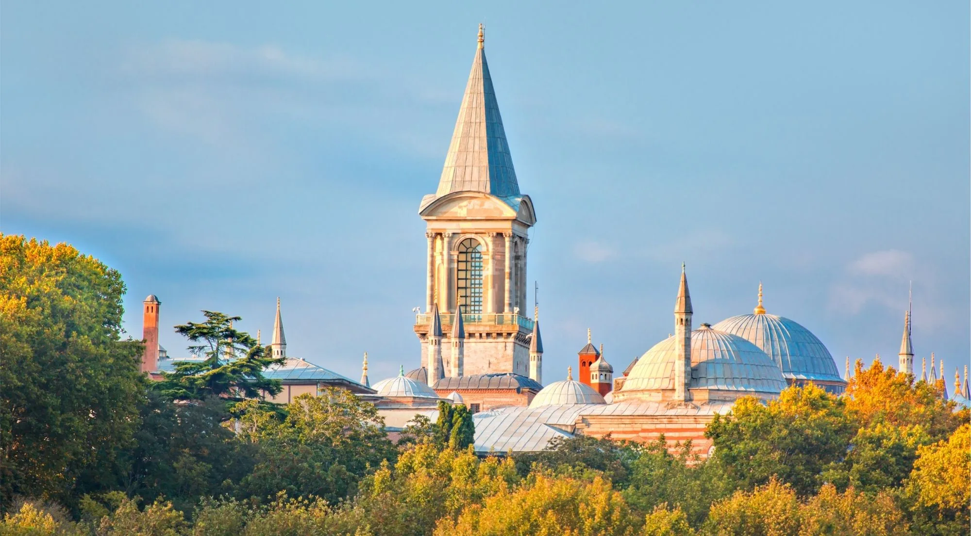 The Tower of Justice rising above the grey lead domes and red chimneys of Topkapi Palace among autumn trees
