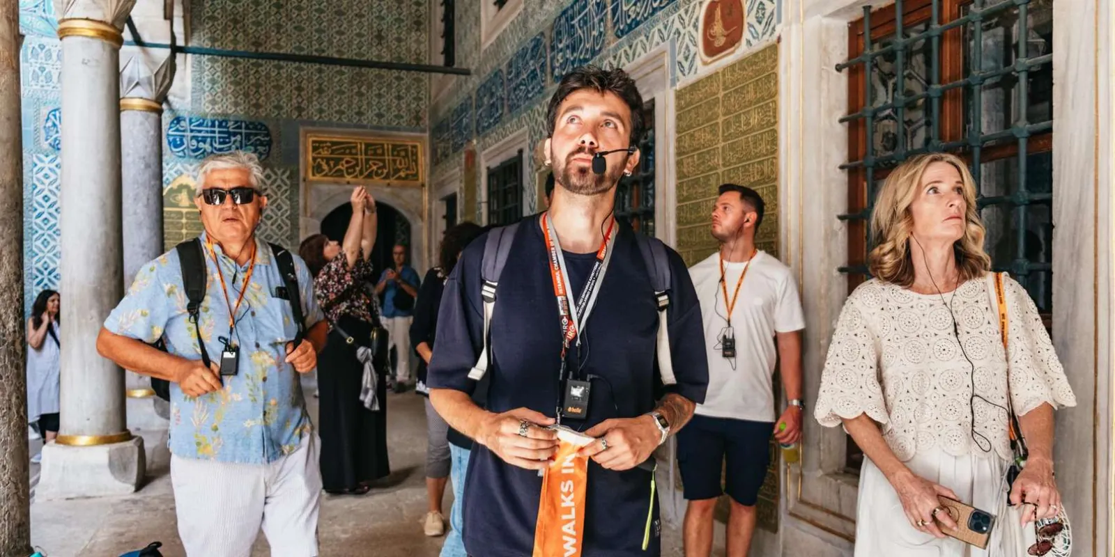A guide with a headset microphone leads a small tour group along a tiled colonnade inside Topkapi Palace