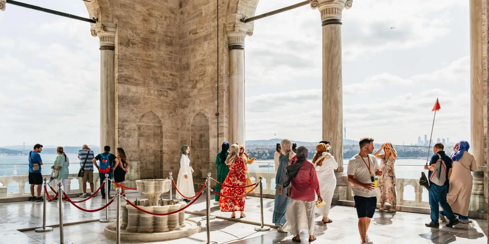Visitors on the marble terrace at Topkapi Palace looking out over the Bosphorus past a fountain and colonnade
