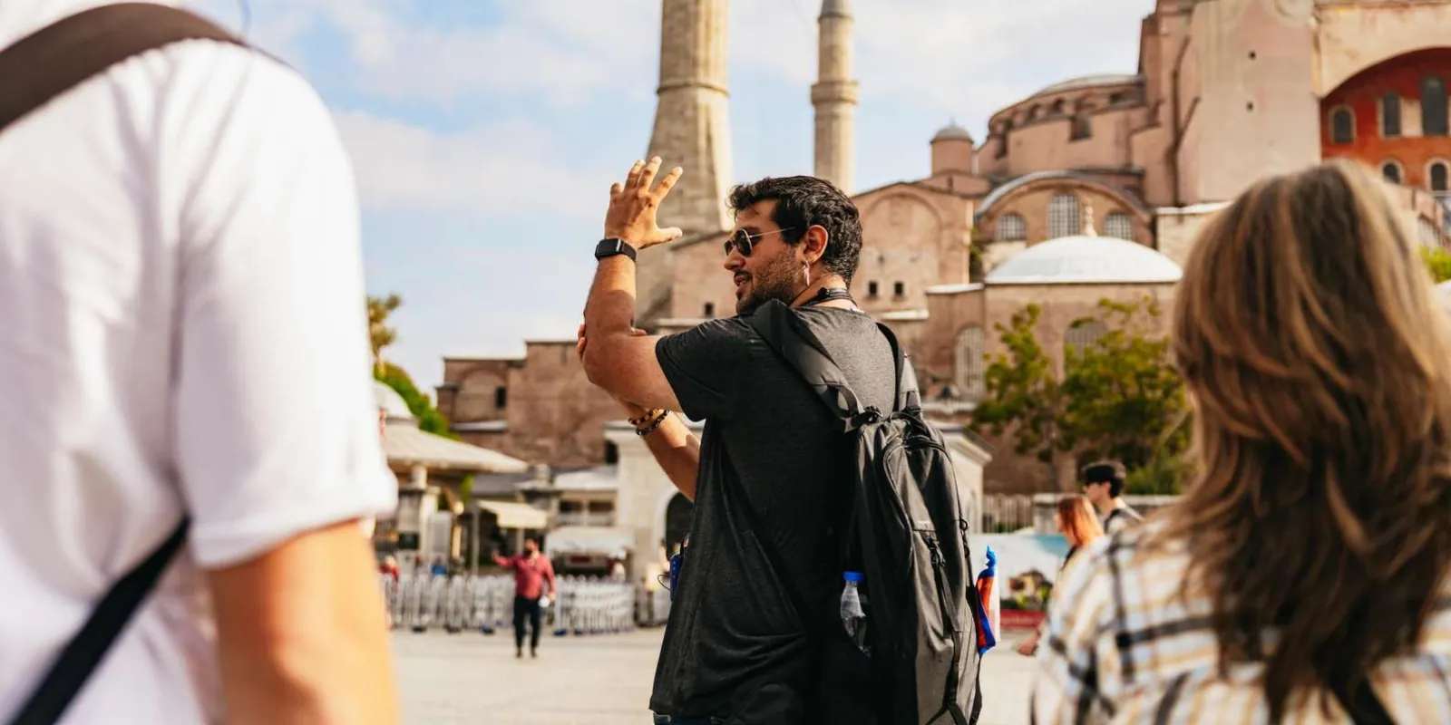 A guide gesturing towards Hagia Sophia while talking to travellers in the square outside
