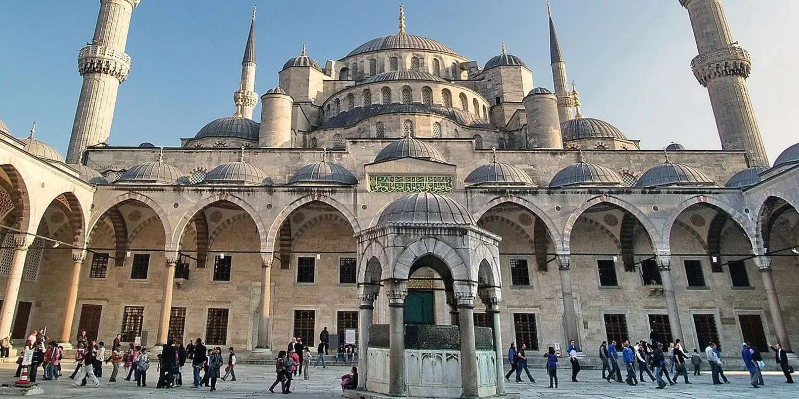 The domed courtyard and six minarets of the Blue Mosque with visitors crossing the flagstones
