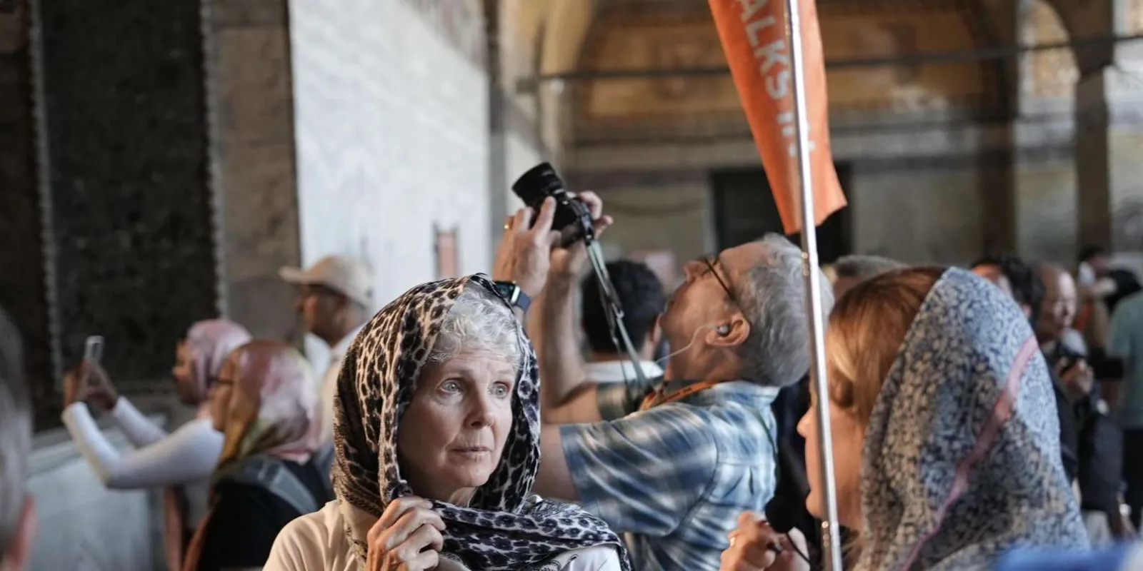 A visitor adjusting her headscarf inside Hagia Sophia as her tour group gathers under the guide's flag