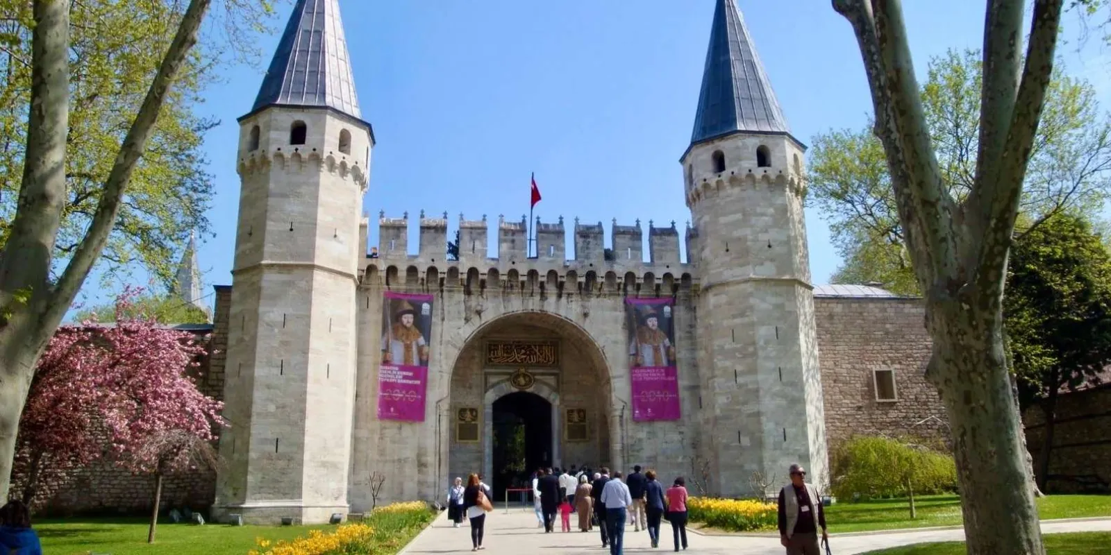 The Gate of Salutation at Topkapi Palace in spring, with blossom and visitors walking up to the arch