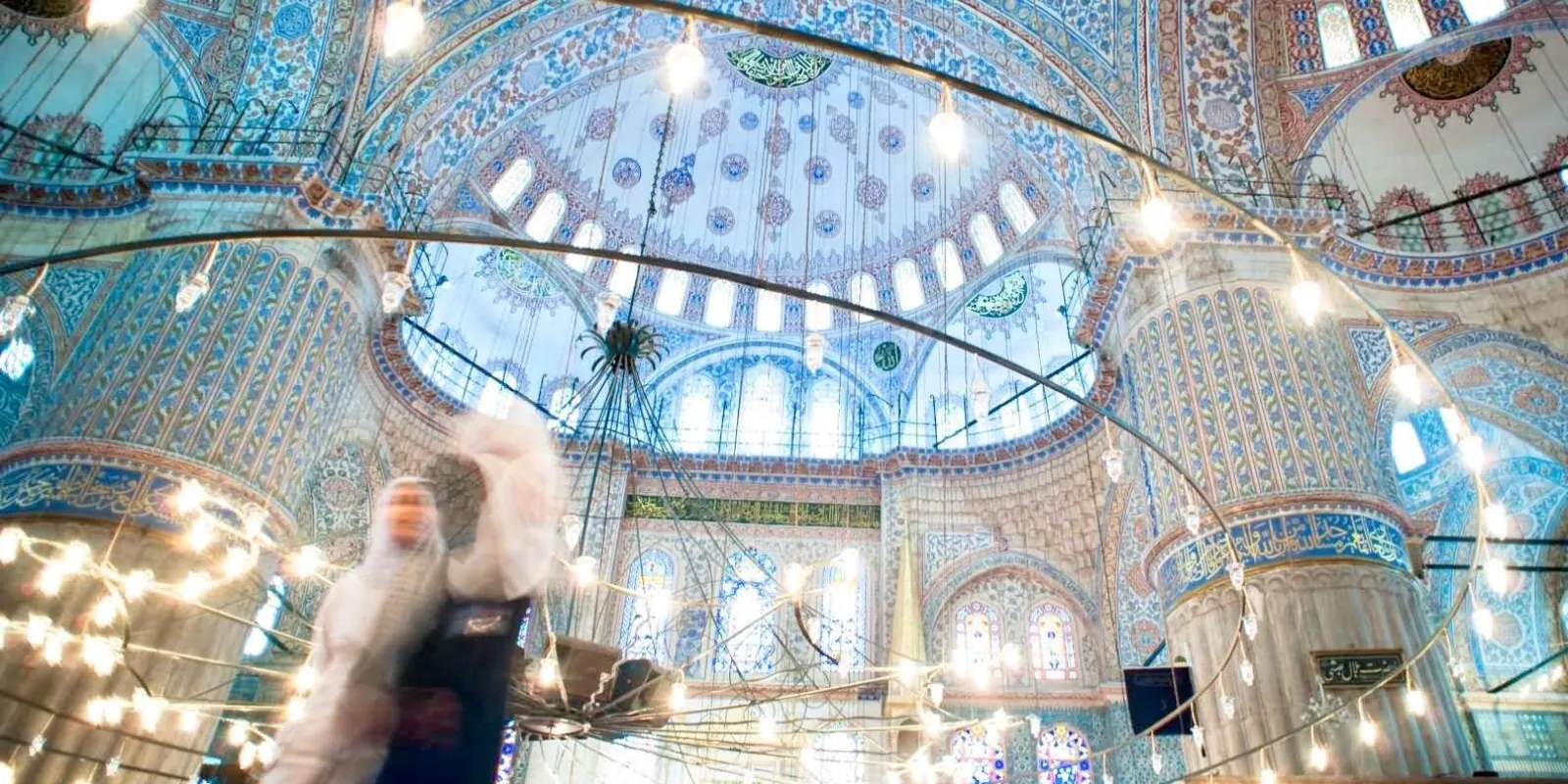 The blue-tiled interior domes and hanging lamps of the Blue Mosque seen from below