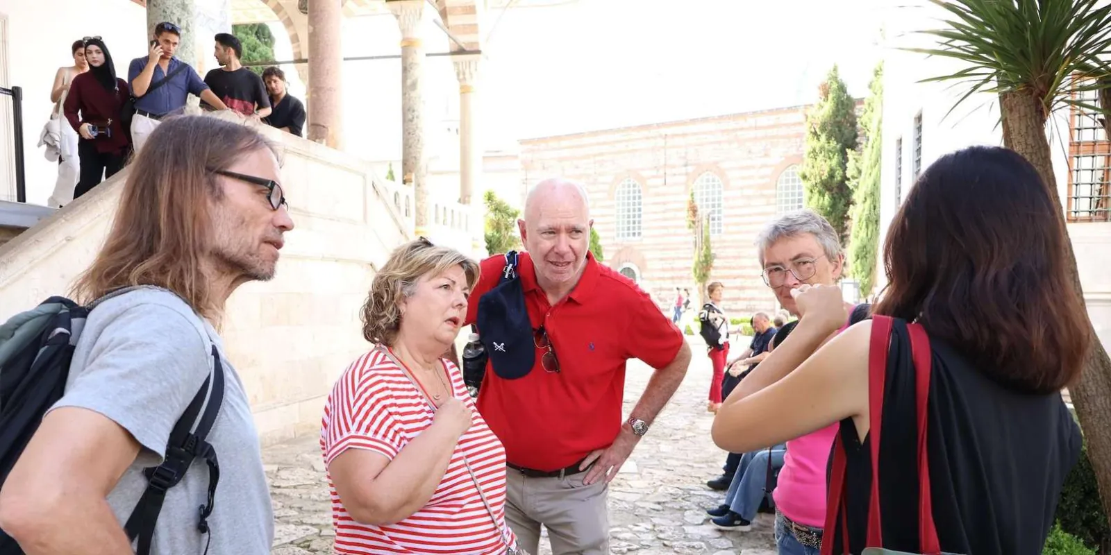 A small tour group listening to their guide beside the steps of a pavilion in Topkapi Palace