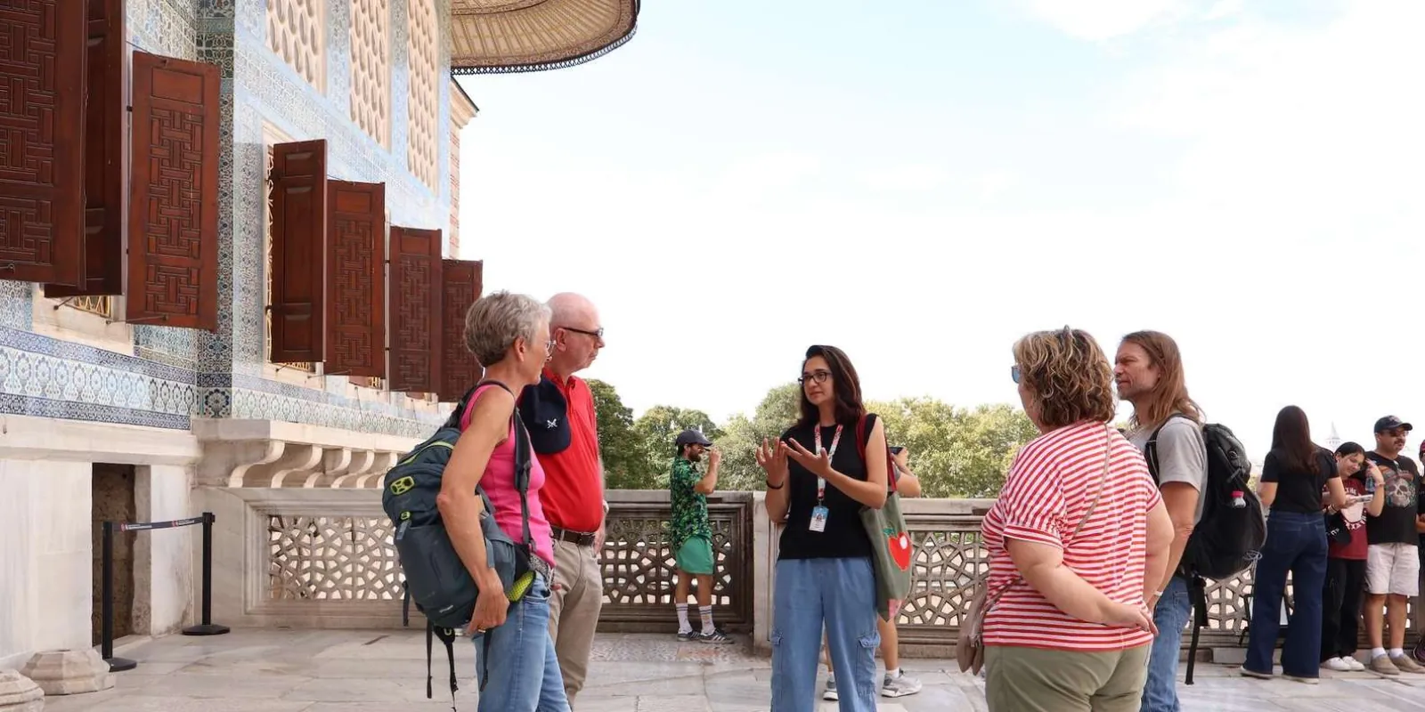 A guide talking to her group on the terrace outside a tiled Topkapi Palace pavilion with wooden shutters