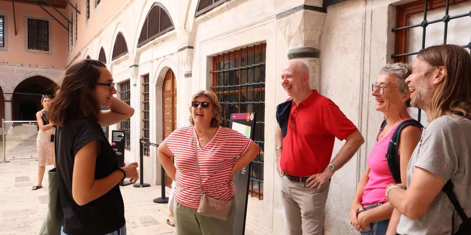 A tour group laughing with their guide in a colonnaded courtyard at Topkapi Palace