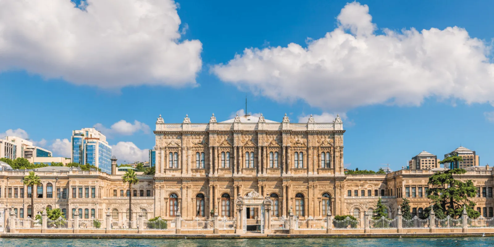 The long Bosphorus-facing facade of Dolmabahce Palace seen from the water under a blue sky